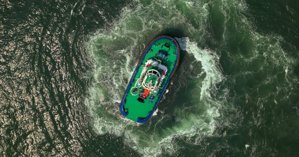 Aerial view of a tug turning in a circle of white water, filmed for Udupi Cochin Shipyard